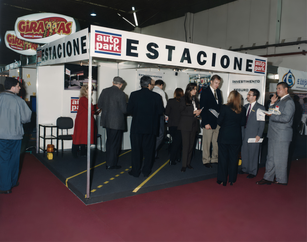 Feira de Franquias com estande da Autopark em ambiente interno, com pessoas em volta do balcão e painéis de divulgação; registro histórico do evento.