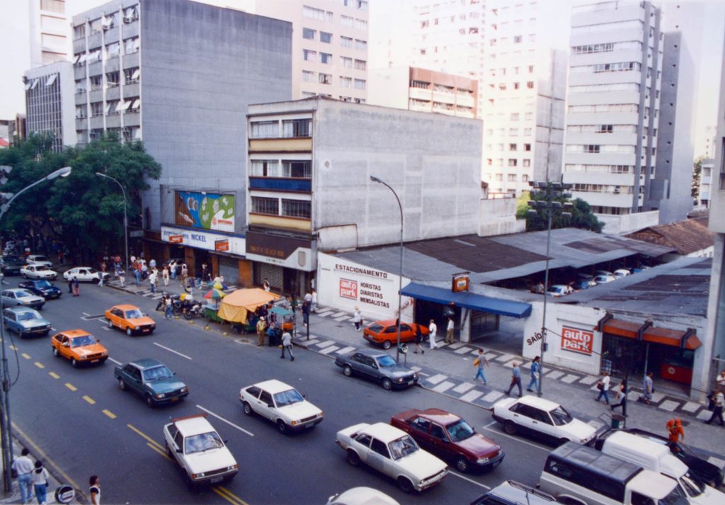 Foto da primeira unidade de estacionamento da autopark no estacionamento Santa Cecília, em área urbana com carros e ônibus na avenida, incluindo sinalização de vagas.