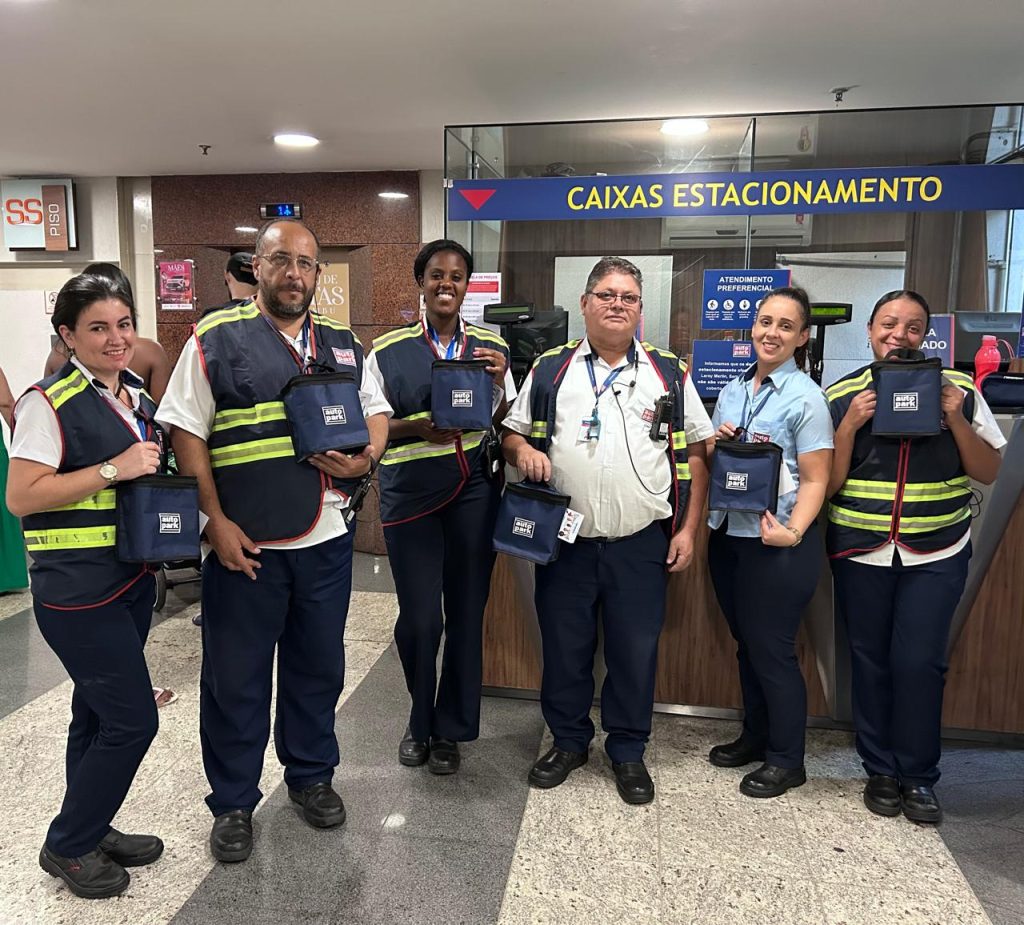 Equipe do time Autopark em atendimento nas caixas de estacionamento, com colaboradores uniformizados e crachás segurando pastas e equipamentos no balcão “CAIXAS ESTACIONAMENTO”.