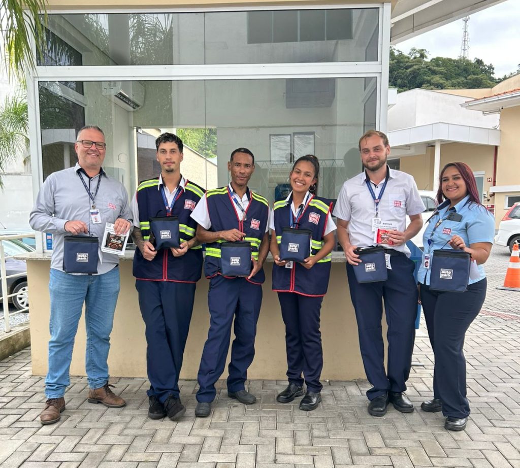 Equipe do time autopark em foto ao ar livre, com seis profissionais uniformizados e crachás, segurando troféus e pastas de premiação em frente a um prédio.