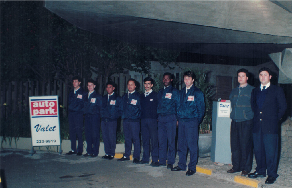 Equipe Autopark em registro de início dos anos 2000, com grupo de funcionários uniformizados em frente à fachada do local, ao lado de placas de Autopark e Valet.