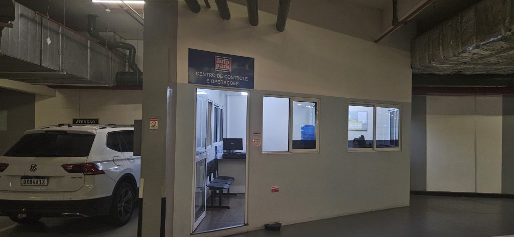 Sala de controle em estacionamento, com acesso por portas de vidro e área interna com vagas ao fundo, mostrando gestão e operação do local para rentabilidade de estacionamento