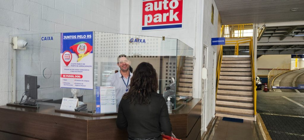 Interior de um estacionamento em shopping, com cabine de atendimento, área de circulação e acesso por escadas com estrutura metálica e sinalização do Autopark.