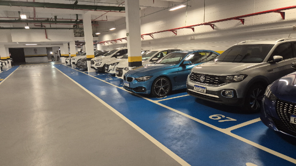 Vista de vagas de estacionamento terceirizado coberto com carros estacionados em fileiras, com faixas de demarcação azul e sinalização no chão.