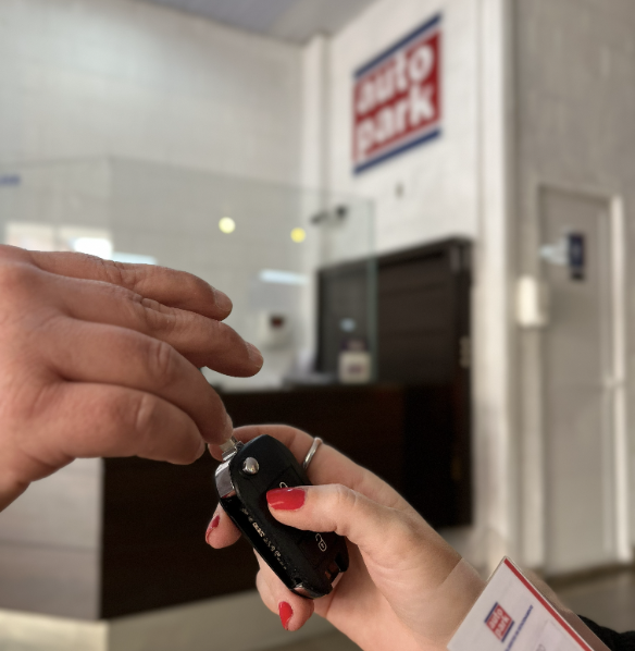 Pessoa usando chave automotiva em mão dentro de um local de atendimento, com área interna desfocada ao fundo e placas de sinalização ao estilo de estacionamento terceirizado.