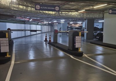 Corredor de estacionamento subterrâneo com vagas demarcadas, barreiras e equipamentos de controle de acesso, representando gestão terceirizada de estacionamento e operação organizada para motoristas.