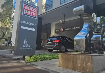 Placa indicativa de estacionamento rotativo comercial com seta e sinalização de segurança em Autopark, em frente a fachada de edifício comercial, com carros no acesso.