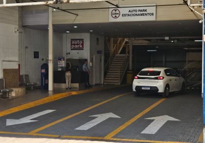 Estacionamento rotativo em shopping com vaga demarcada e entrada do Autopark, com carro no corredor e sinalização de orientação ao fundo.